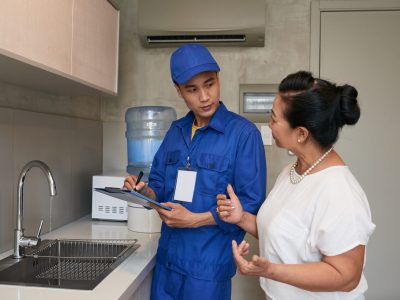 Mature Vietnamese woman talking to plumber in her kitchen